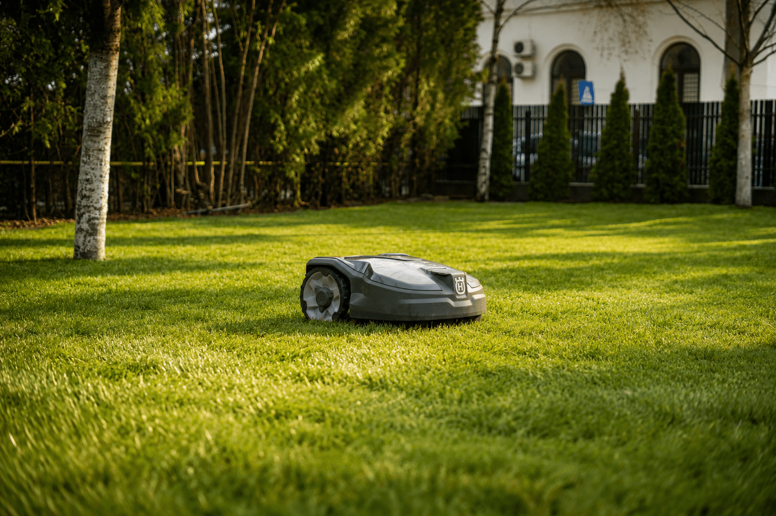 Robot de tuns gazonul pe o peluză verde cu arbori și gard viu